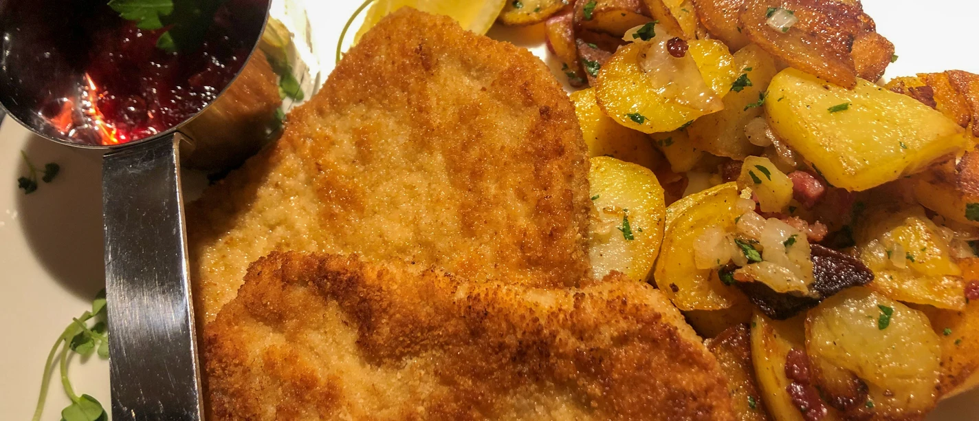 Zwei goldbraun panierte Wiener Schnitzel mit Zitronenscheibe, Preiselbeersoße und Bratkartoffeln.