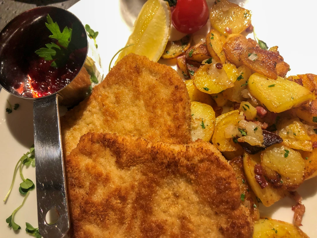 Essen_Wiener_Schnitzel_SHS_CC-BY-SA_Teutoburger_Wald_Stadt_Schloss_Holte-Stukenbrock (1).jpg Zwei goldbraun panierte Wiener Schnitzel mit Zitronenscheibe, Preiselbeersoße und Bratkartoffeln.