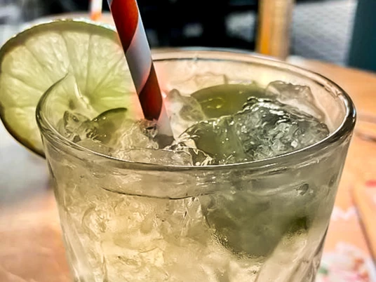 Erfrischende limonadengrüne Getränkeglas mit Eiswürfeln, Limettenscheibe und gestreiftem Strohhalm.