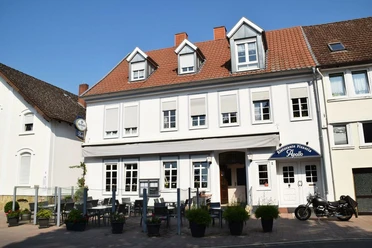 Restaurant Apollo.JPG Das Bild zeigt ein großes Restaurantgebäude mit roten Dachziegeln und einer Außenterrasse bei Sonnenschein.