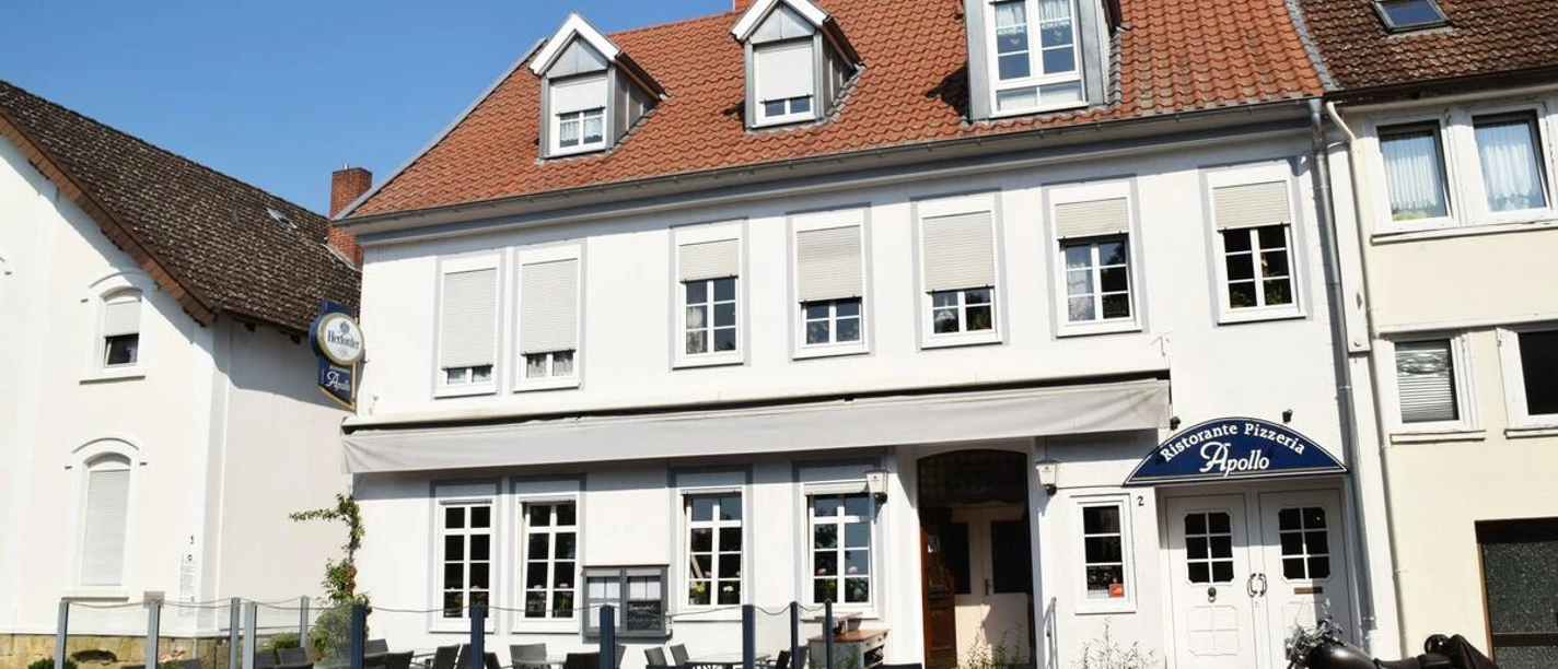 Restaurant Apollo.JPG Das Bild zeigt ein großes Restaurantgebäude mit roten Dachziegeln und einer Außenterrasse bei Sonnenschein.