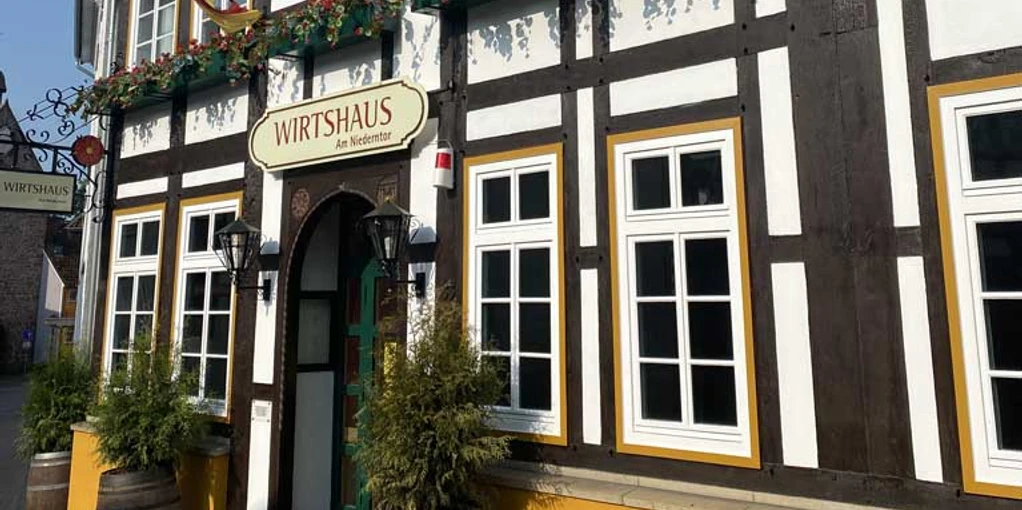 Historisches Fachwerkhaus mit Schild "Wirtshaus", Blumendekoration und hölzernem Eingangsbogen.