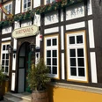 Historisches Fachwerkhaus mit Schild "Wirtshaus", Blumendekoration und hölzernem Eingangsbogen.