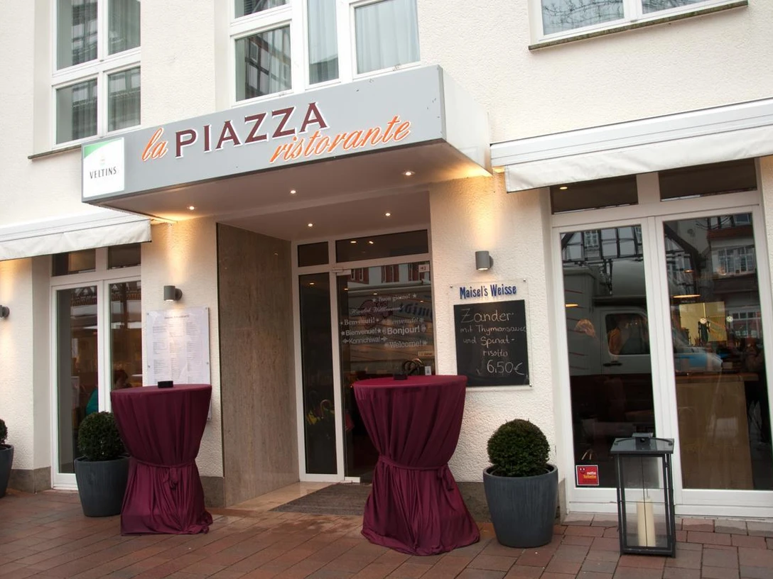 Eingangsbereich zum Restaurant mit Vordach und zwei Rundtischen, dekoriert mit roten Tüchern.