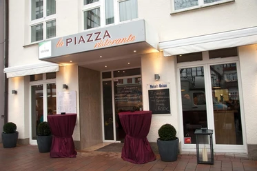La Piazza Ristorante.JPEG Eingangsbereich zum Restaurant mit Vordach und zwei Rundtischen, dekoriert mit roten Tüchern.