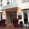 La Piazza Ristorante.JPEG Eingangsbereich zum Restaurant mit Vordach und zwei Rundtischen, dekoriert mit roten Tüchern.