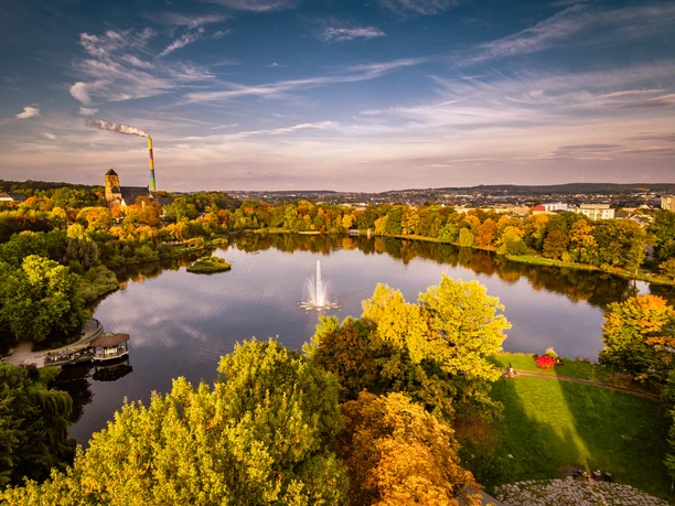 Schlossteich1_chemnitz-von-oben.de_CWE.jpg Herbstlich gefärbter Schlossteich in Chemnitz, mit zentralem Springbrunnen und umliegenden Bäumen.
