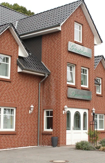 Rotes Backsteingebäude mit dunkelgrauem Schrägdach, Gasthaus-Schildern und weißer Eingangstür.