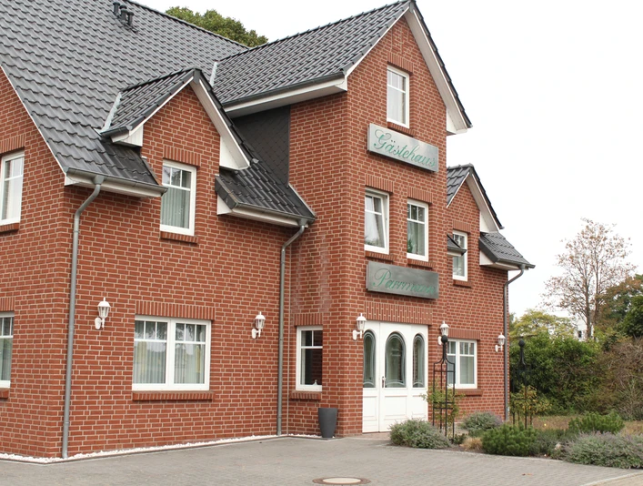 Parrmann Rotes Backsteingebäude mit dunkelgrauem Schrägdach, Gasthaus-Schildern und weißer Eingangstür.