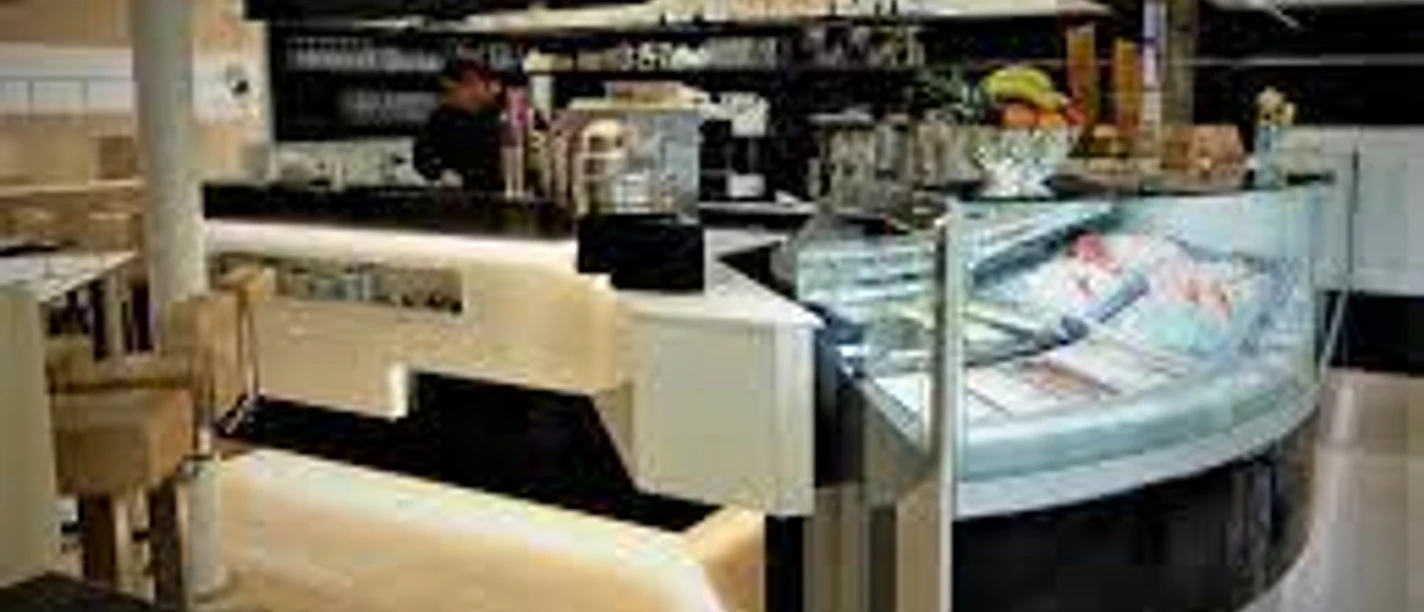 Innenansicht eines modernen Eiscafés mit beleuchtetem Tresen, Glastheke und verschiedenen Eiscremesorten.