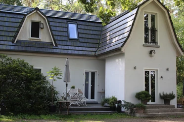 Een klein wit huis met een blauw dak, omringd door bomen en een patio.