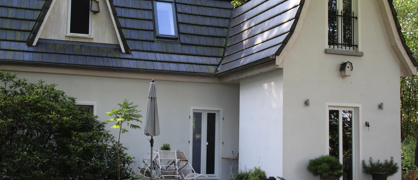 Een klein wit huis met een blauw dak, omringd door bomen en een patio.