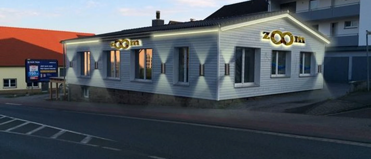 Ein einstöckiges Gebäude mit „zoom“ Beschriftung, das von warmem Kunstlicht bestrahlt wird.