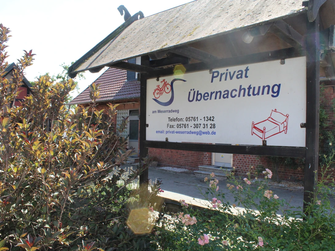 Privat Übernachtung, Müsleringen Schild vor einem Gebäude mit der Aufschrift "Privat Übernachtung" und einem blühenden Busch im Vordergrund.