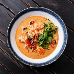 Ein Teller mit thailändischer Garnelensuppe, garniert mit Koriander und Chilischote, auf Holztisch.