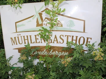 Mühlengasthof, Landesbergen Ein mit grünen Blättern teilverdeckt stehendes Schild mit der Aufschrift "Mühlengasthof, Landesbergen".A sign partially covered with green leaves with the inscription "Mühlengasthof, Landesbergen".Et skilt delvist dækket af grønne blade med påskriften "Mühlengasthof, Landesbergen".Een bord gedeeltelijk bedekt met groene bladeren met de inscriptie "Mühlengasthof, Landesbergen".