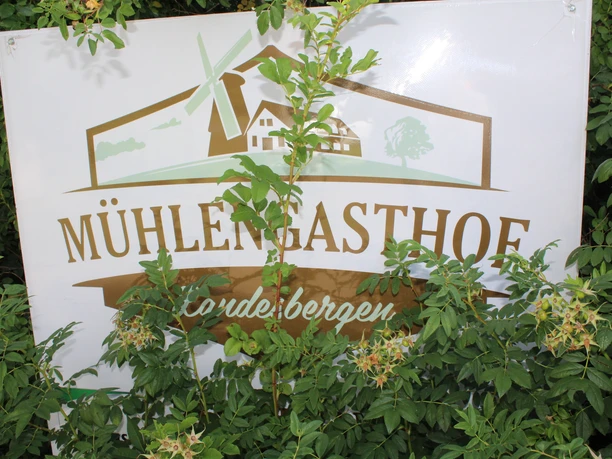 Mühlengasthof, Landesbergen Ein mit grünen Blättern teilverdeckt stehendes Schild mit der Aufschrift "Mühlengasthof, Landesbergen".