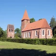St. Ulrichs-Kirche - Seitenansicht mit Turm Backsteinkirche mit hohem Turm und rotem Ziegeldach, umgeben von grünen Bäumen und Rasenfläche.