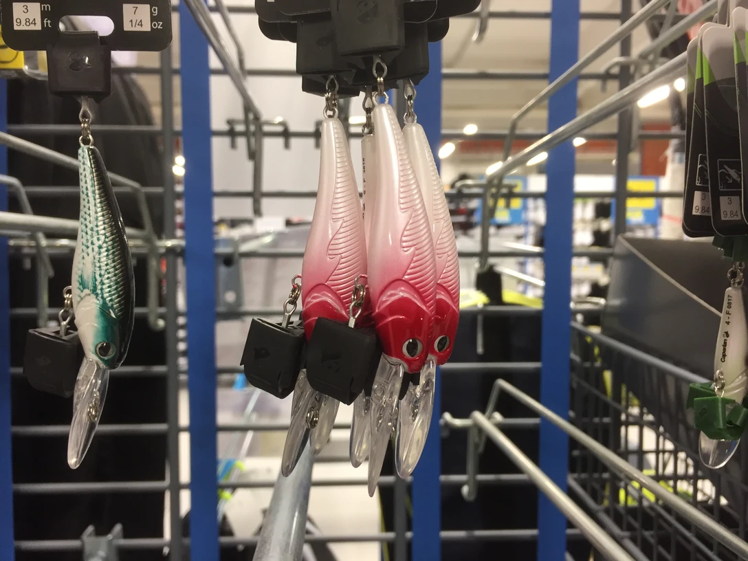 angeln11.JPG Verschiedenfarbige Angelköder in einem Geschäft, organisiert an einem Metallständer mit Details sichtbar.