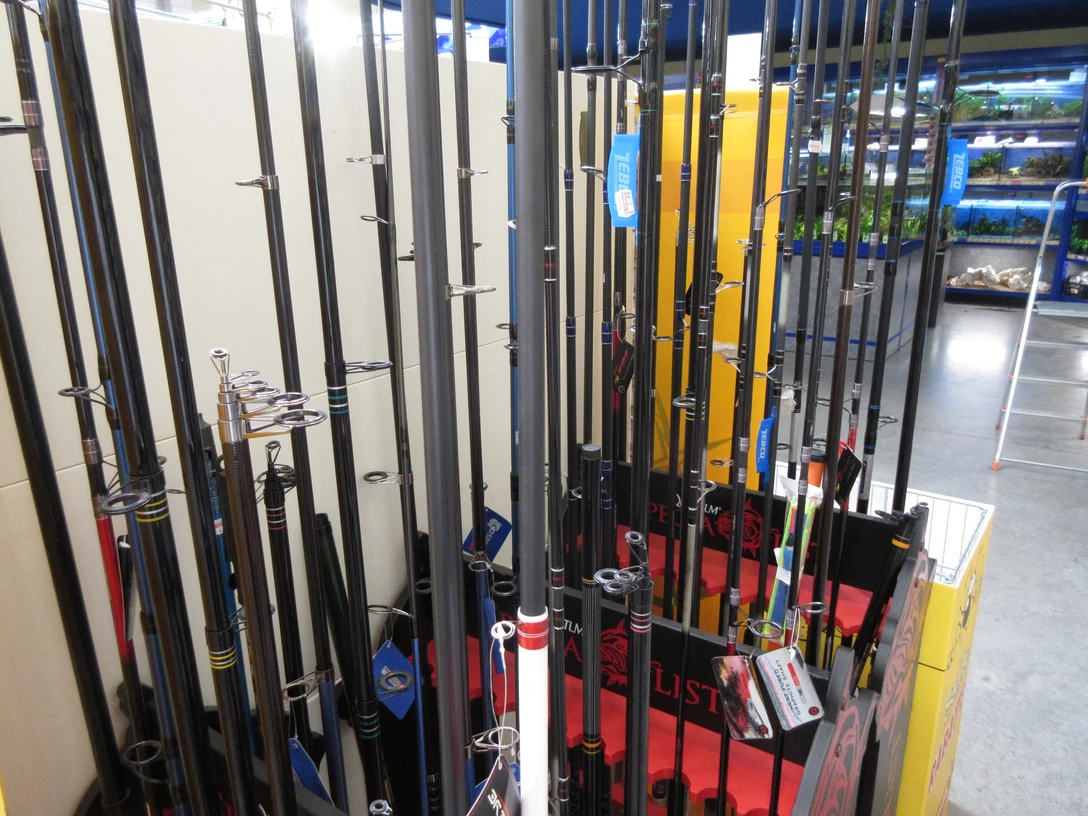 Angelzubehör (2).JPG Verschiedene Angelruten stehen aufrecht in einem Innenraum. Im Hintergrund sind blaue Aquarien zu sehen.