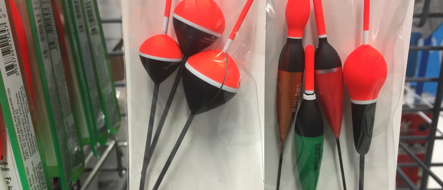 In einem Anglergeschäft hängen in Folien verpackte bunte Schwimmer verschiedener Formen und Größen.