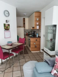 Küche & Esszimmer, Apartment Judt NEU Modern eingerichtete Küche mit hellem Holz, kleinem Esstisch mit roten Stühlen und Glasvitrine.