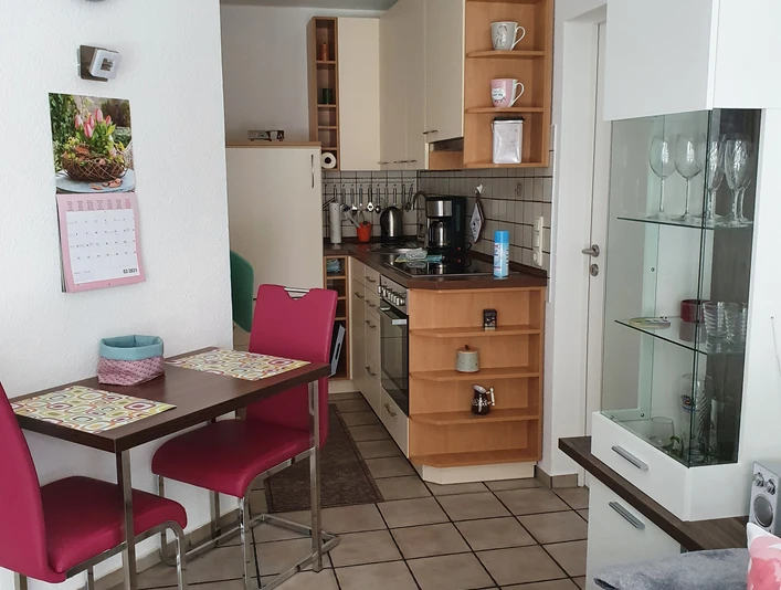 Küche & Esszimmer, Apartment Judt NEU Modern eingerichtete Küche mit hellem Holz, kleinem Esstisch mit roten Stühlen und Glasvitrine.