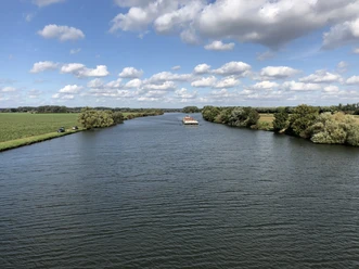 Weser, Landesbergen (3).jpg Breitflächiger Fluss, gesäumt von üppigem Grün, unter strahlend blauem Himmel mit ziehenden Wolken.