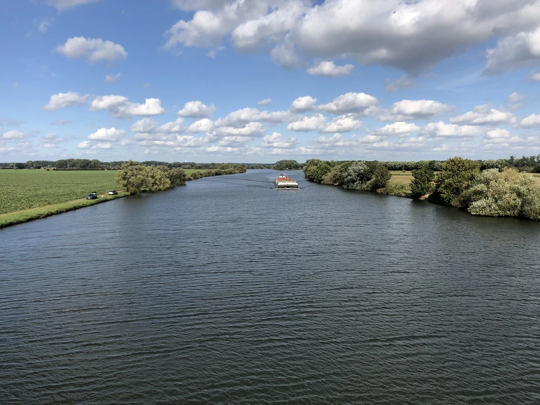 Weser, Landesbergen (3).jpg Breitflächiger Fluss, gesäumt von üppigem Grün, unter strahlend blauem Himmel mit ziehenden Wolken.