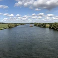 Weser, Landesbergen (3).jpg Breitflächiger Fluss, gesäumt von üppigem Grün, unter strahlend blauem Himmel mit ziehenden Wolken.