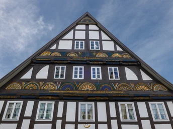 Fachwerkhaus mit verziertem Giebel und weißen Fenstern, eingerahmt von einem blauen Himmel.