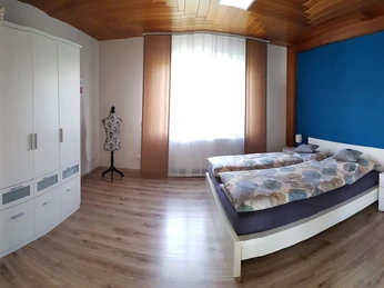 Schlafzimmer Ein helles Schlafzimmer mit einem Doppelbett, weißen Möbeln, Parkettboden und einem Fenster mit Vorhängen.