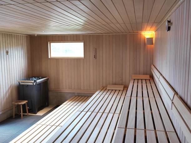 Aqualip Saunaland Innenansicht einer Holzsauna mit Bänken, einem kleinen Fenster und einem Ofen für Wärme.