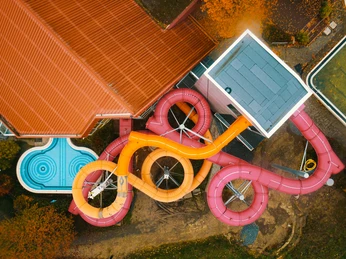 Aqualip Freizeitbad Zwei ineinander verschlungene Wasserrutschen in leuchtendem Orange und Pink neben einem Schwimmbecken.