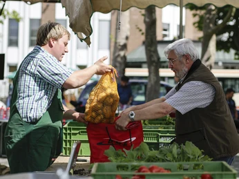 20130719hs0248.jpg Ein Verkäufer übergibt einem älteren Mann einen Sack Kartoffeln auf einem belebten Wochenmarkt.