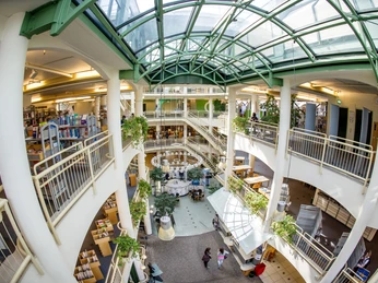 Stadtbibliothek Gütersloh. Eine lichtdurchflutete Bibliothek mit Glasdach, Pflanzen und offenen Büchergalerien auf mehreren Etagen.