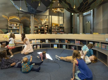 Kinder lesen und spielen in einer gemütlichen Bibliothek mit runden Regalen und verspieltem Dekor.