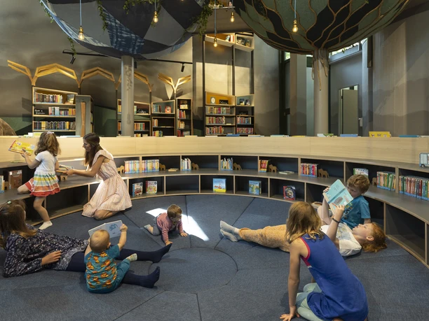 Kinderecke Stadtbibliothek Gütersloh Kinder lesen und spielen in einer gemütlichen Bibliothek mit runden Regalen und verspieltem Dekor.