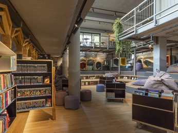 Ein einladender, moderner Bibliotheksraum mit gemütlichen Sitzkissen und Regalen voller Bücher.