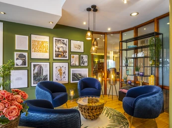 Aufenthaltsbereich Mercure Hotel Ein stilvoller Raum mit blauen Sesseln, grüner Wandgalerie und warmem Licht, das eine einladende Atmosphäre schafft.