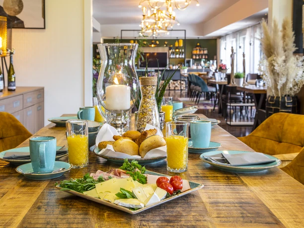 Beispiel Frühstückstisch Ein reichhaltig gedeckter Frühstückstisch mit Brötchen, Aufschnitt, Orangensaft und Kaffee im wohnlichen Ambiente.