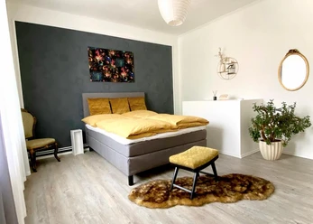 9 Quellen City Apartment.jpg Modern eingerichtetes Schlafzimmer mit Doppelbett, Sitzhocker, Pflanzen und Wanddekorationen.