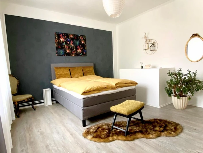 9 Quellen City Apartment.jpg Modern eingerichtetes Schlafzimmer mit Doppelbett, Sitzhocker, Pflanzen und Wanddekorationen.