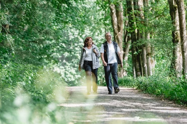 Geführte Wanderung Zwei Personen spazieren auf einem Waldweg, umgeben von dichtem grünen Blattwerk.