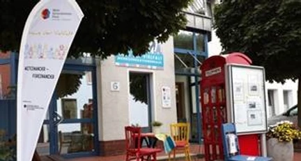 MGH.jpg Ein Treffpunkt mit bunten Stühlen und Tischen vor dem Mehrgenerationenhaus und einer roten Telefonzelle.