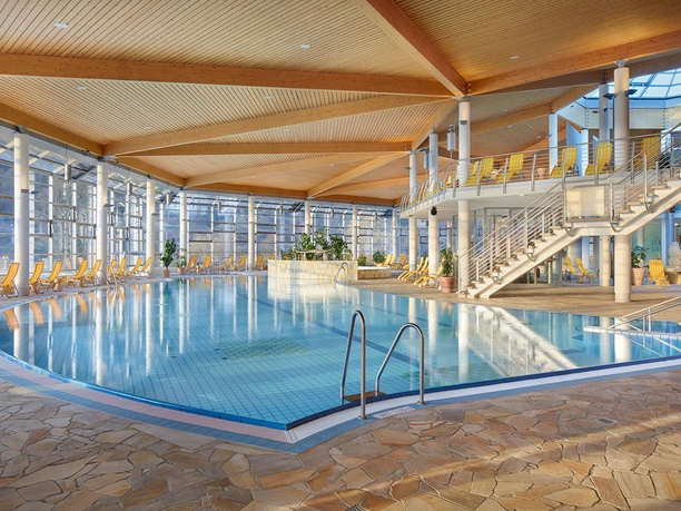 Toskana Therme Innenbereich Toskana Therme Bad Schandau: Helles Hallenbad mit blauem Wasser, umgeben von gelben Liegestühlen und großen Fenstern; moderne, luftige Atmosphäre mit Holzdecke.