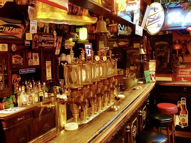 brösel.jpg Traditionelle Kneipe mit historischen Schildern, langer Holztheke und Zapfanlage, umgeben von Barhockern.