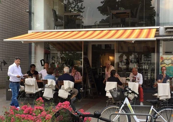 501_212168432.jpg Menschen genießen Speisen unter einem gestreiften Sonnendach vor einem Café, Fahrräder im Vordergrund.