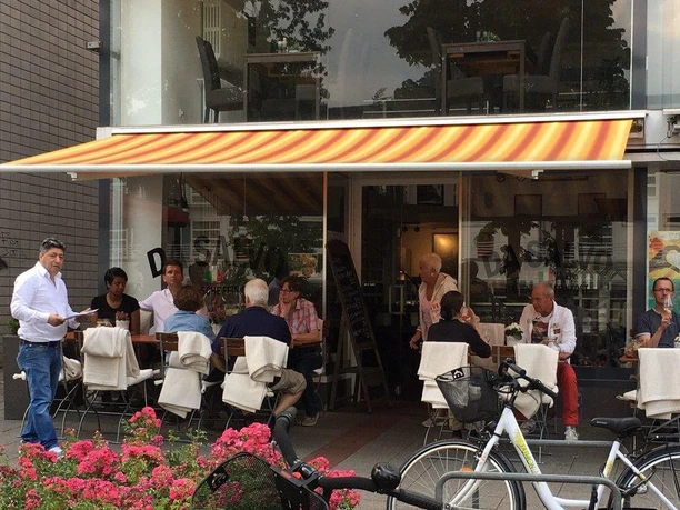 501_212168432.jpg Menschen genießen Speisen unter einem gestreiften Sonnendach vor einem Café, Fahrräder im Vordergrund.