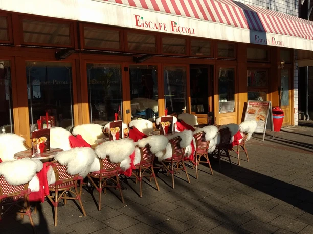 28616543_1876379535705811_6119886081932960166_o.jpg Das Bild zeigt den Außenbereich des Eiscafes PiccolIis. Man erkennt viele gemütliche Sitzgelegenheiten.